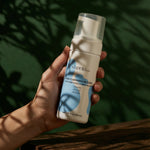 Hand holding a bottle of Shveta Naturals Face Cleansing Mousse against a green leafy background