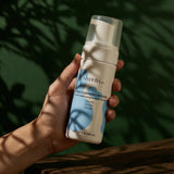 Hand holding a bottle of Shveta Naturals Face Cleansing Mousse against a green leafy background