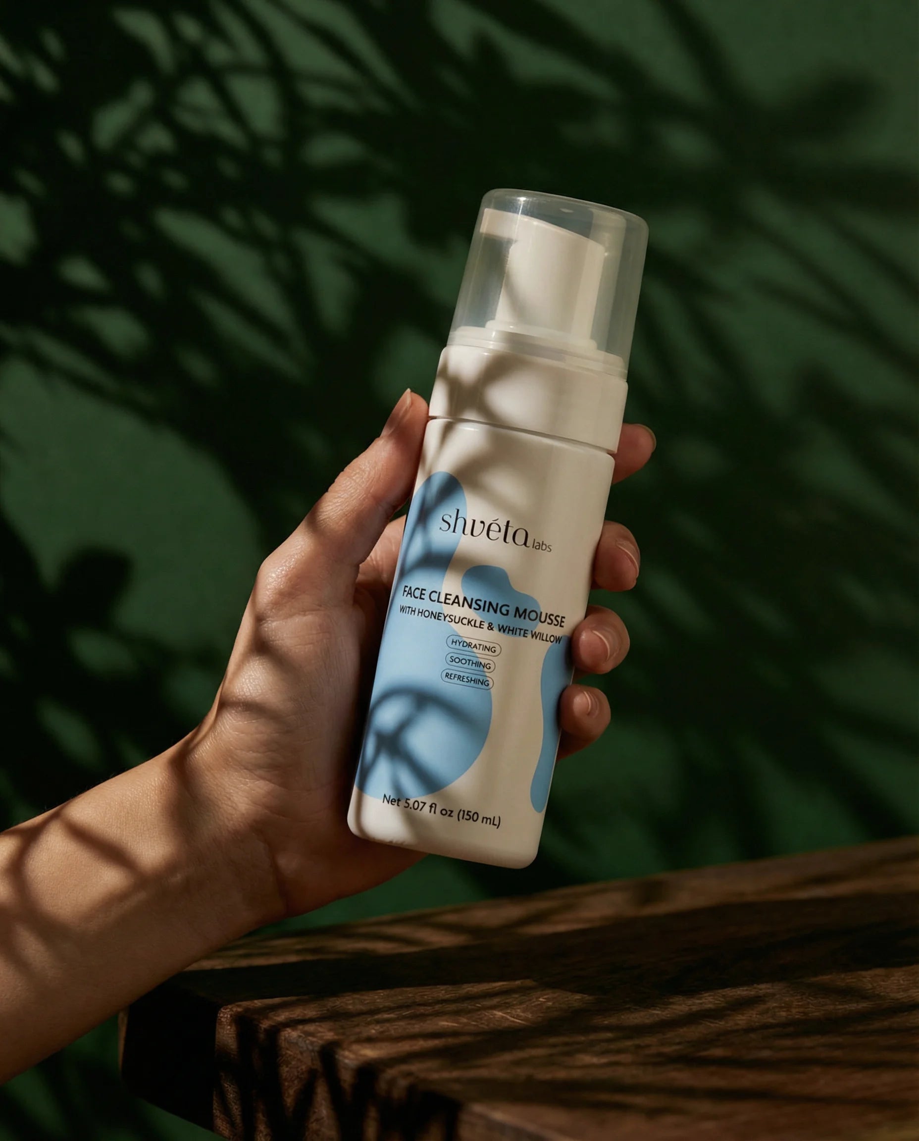 Hand holding a bottle of Shveta Naturals Face Cleansing Mousse against a green leafy background